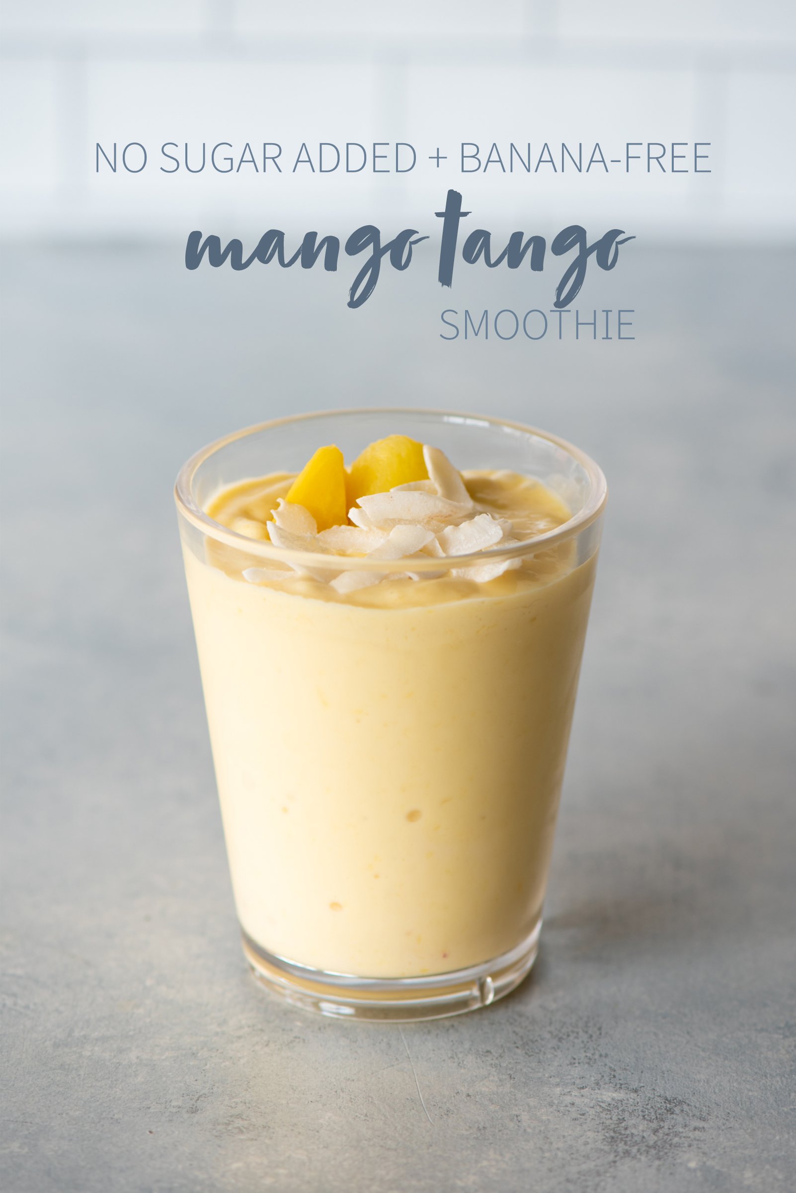 Mango Tango smoothie in a clear glass topped with mango and coconut. A text overlay reads "No Sugar Added + Banana-Free Mango Tango Smoothie."