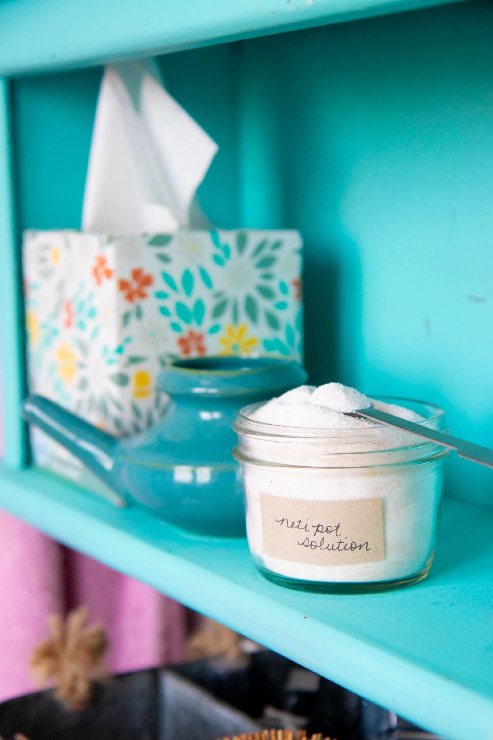 Glass canning jar filled with DIY neti pot solution on a shelf next to a neti pot and a box of tissues.