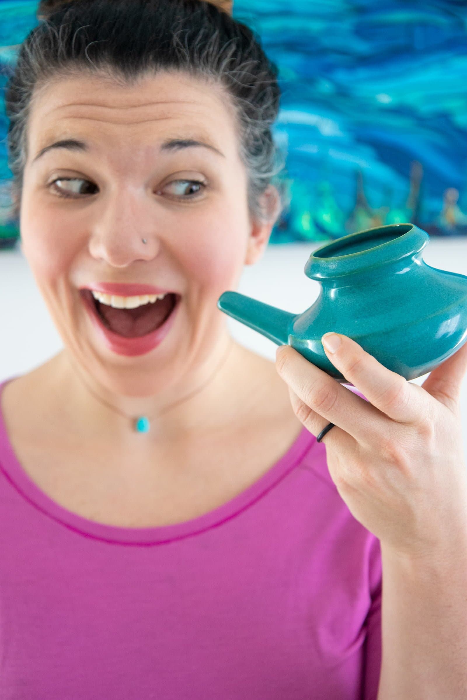 Woman in a pink shirt holding a ceramic neti pot and smiling