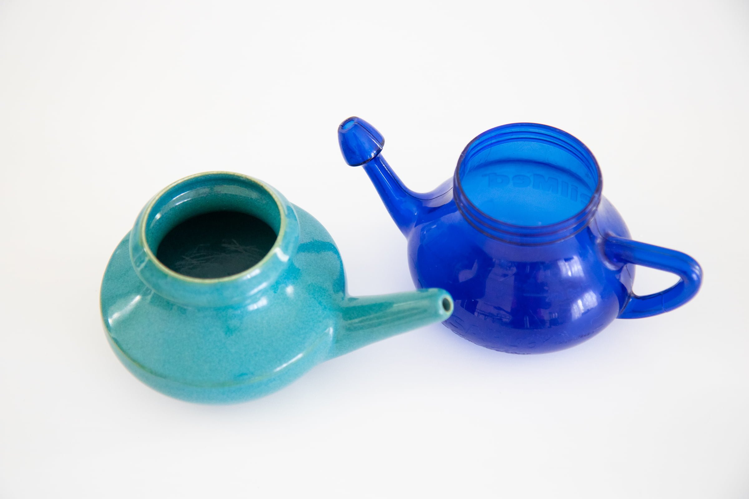 Ceramic neti pot next to a blue plastic neti pot.