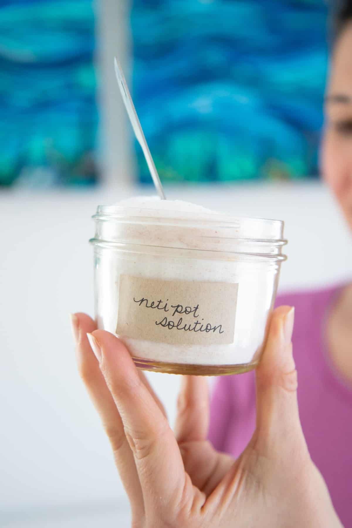 Woman's hand holding a glass canning jar full of DIY neti pot solution.