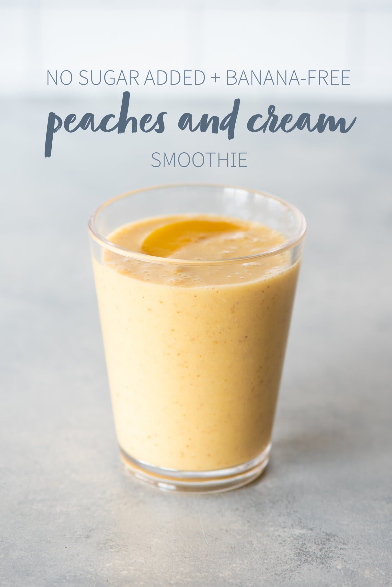 Peaches and cream smoothie in a clear glass topped with sliced peaches. A text overlay reads "No Sugar Added + Banana-Free Peaches and Cream Smoothie."