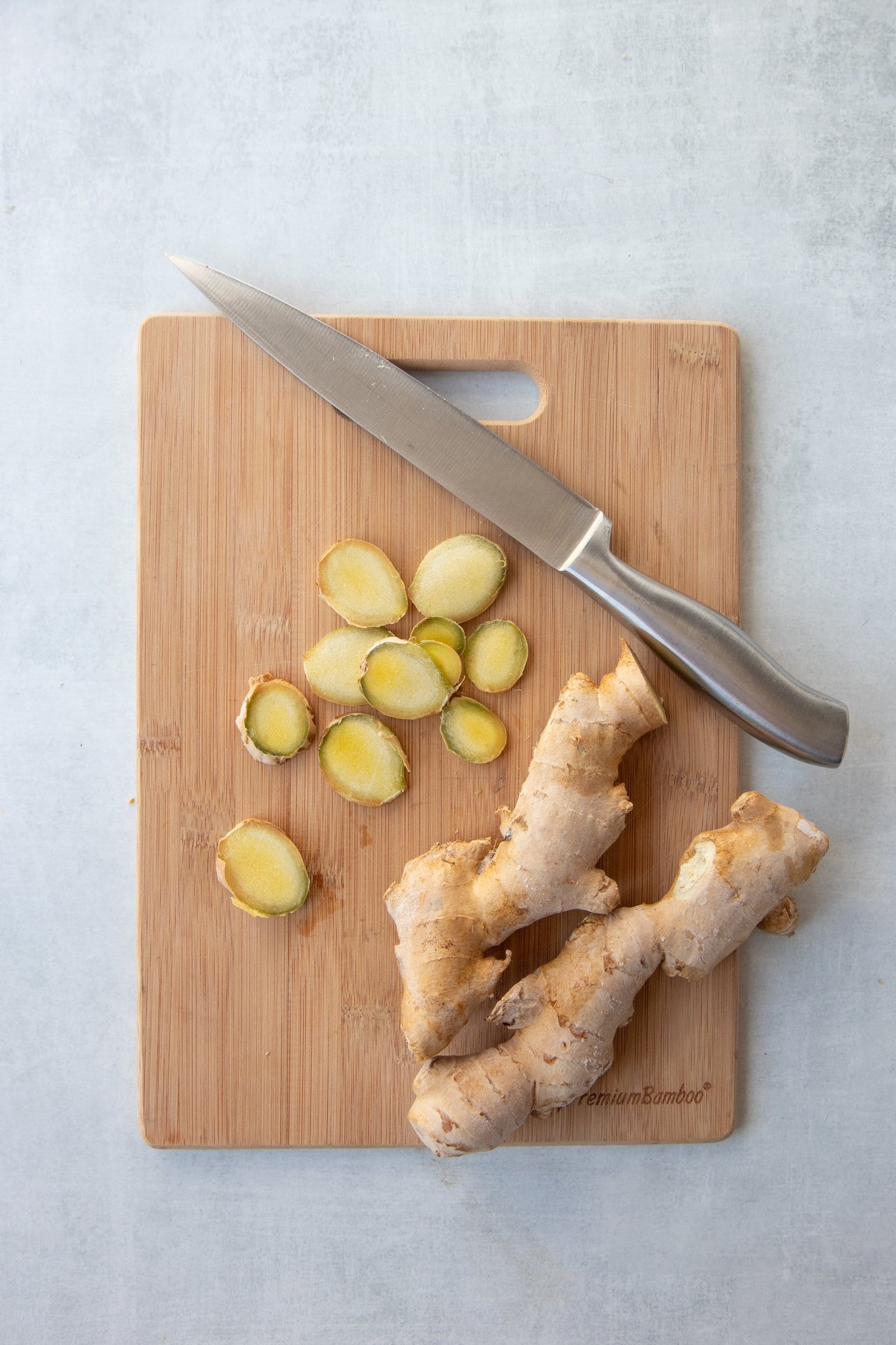 Sliced ginger root and a knife on a wooden cutting board.