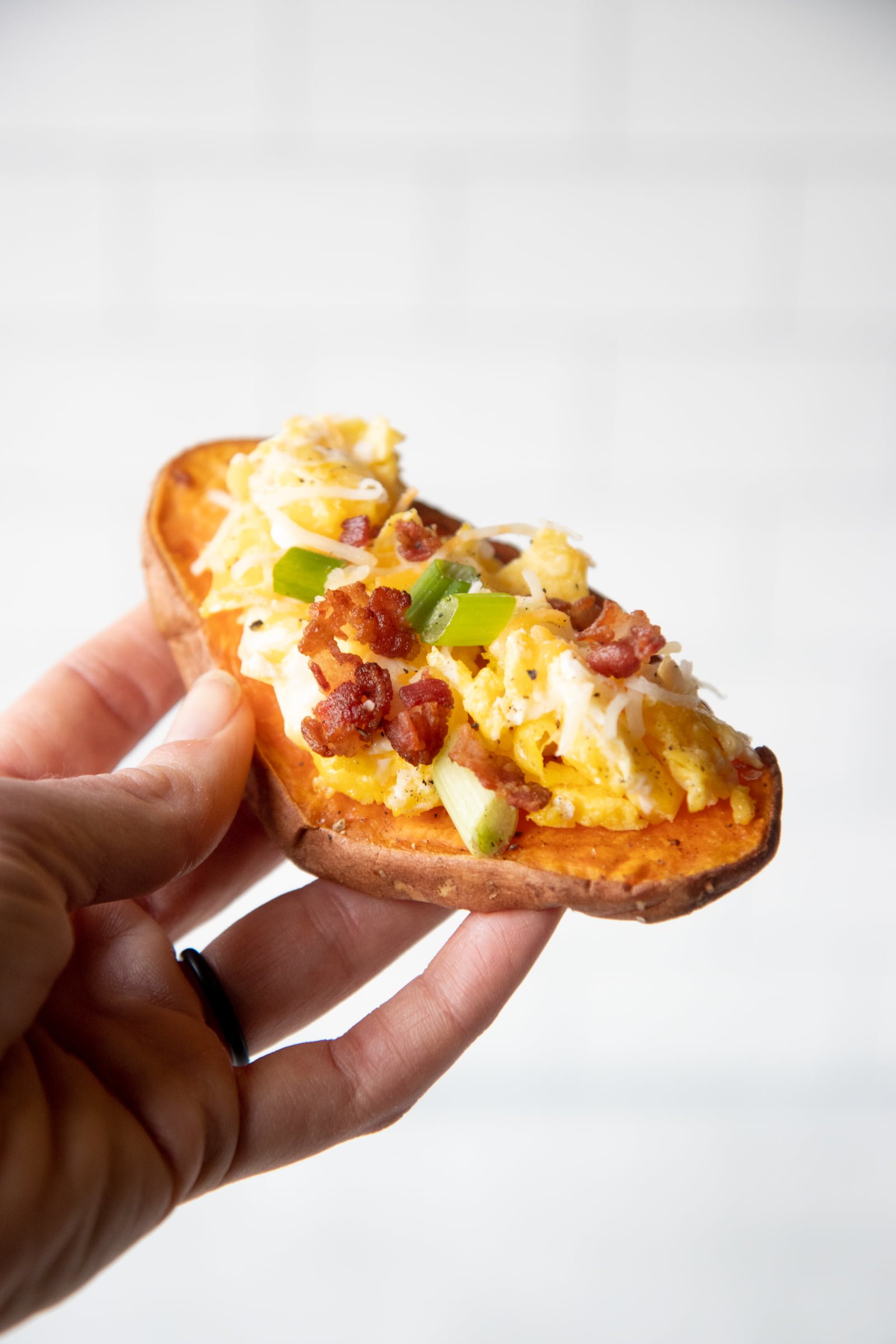 Hand holding a piece of sweet potato toast with bacon and eggs