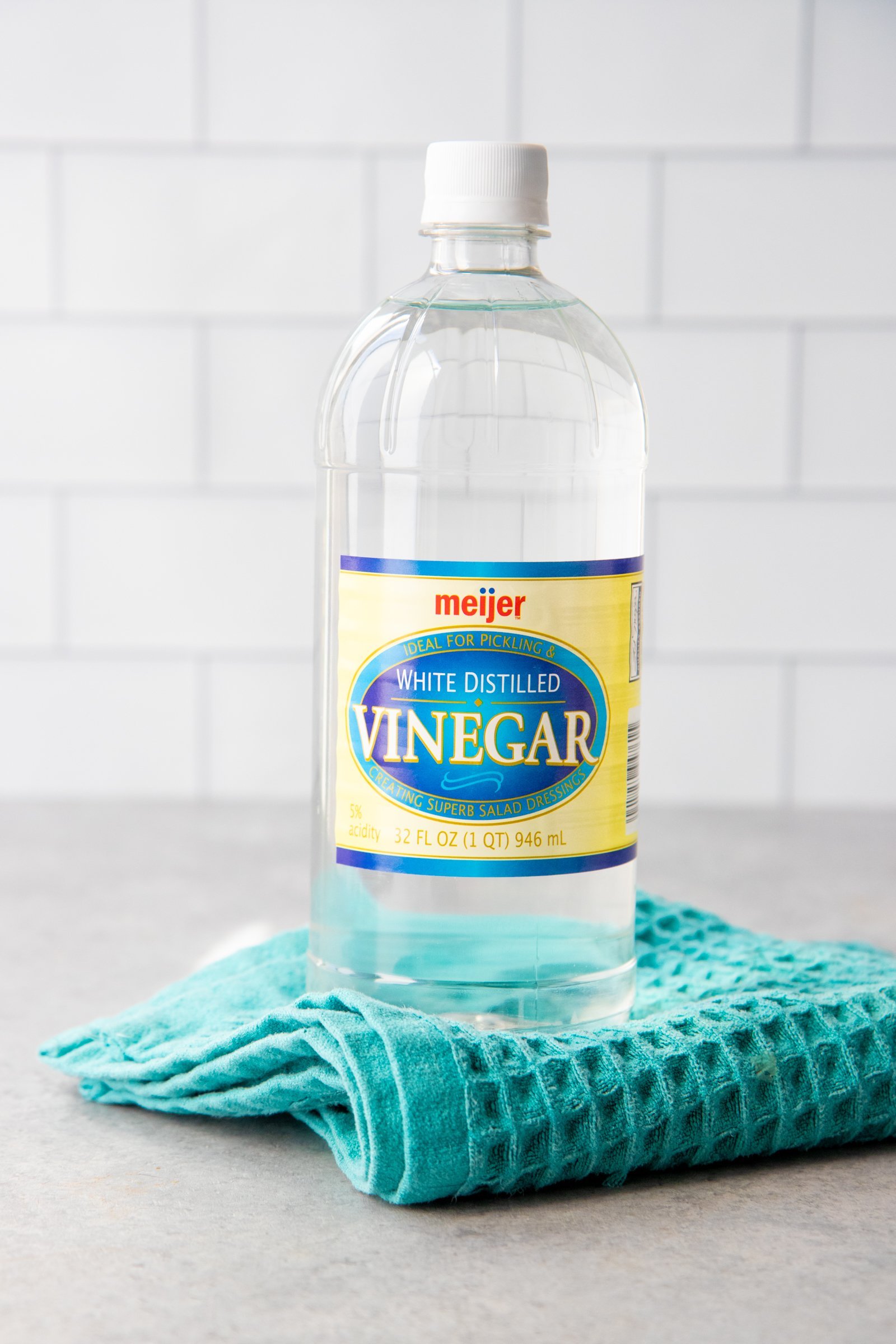 Bottle of distilled white vinegar sitting on top of a teal dish towel.