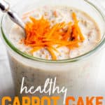 A glass jar filled with carrot cake overnight oatmeal sits on a marble countertop. The oats are garnished with shredded carrots, and a spoon dips into the jar. A text overlay reads "Healthy Carrot Cake Overnight Oats."
