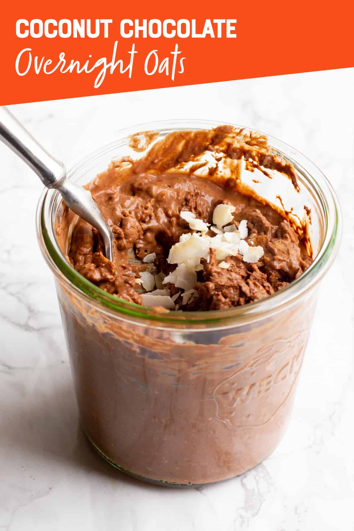 A clear glass jar filled with chocolate coconut overnight oats, with a spoon sticking out. A text overlay reads "Coconut Chocolate Overnight Oats."