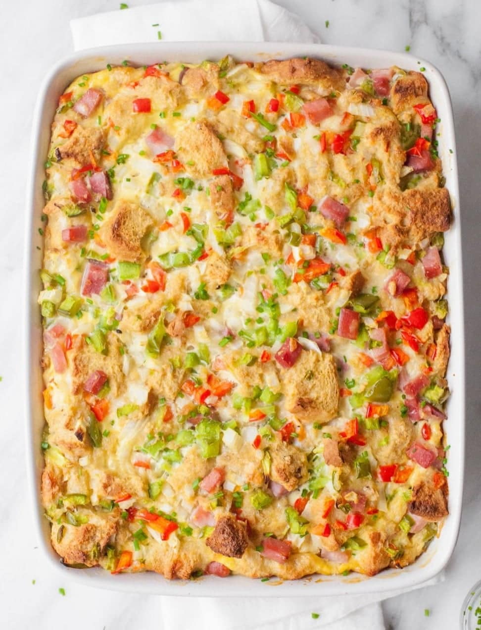 Close view of a breakfast bake studded with red and green peppers, ham, and bread cubes.