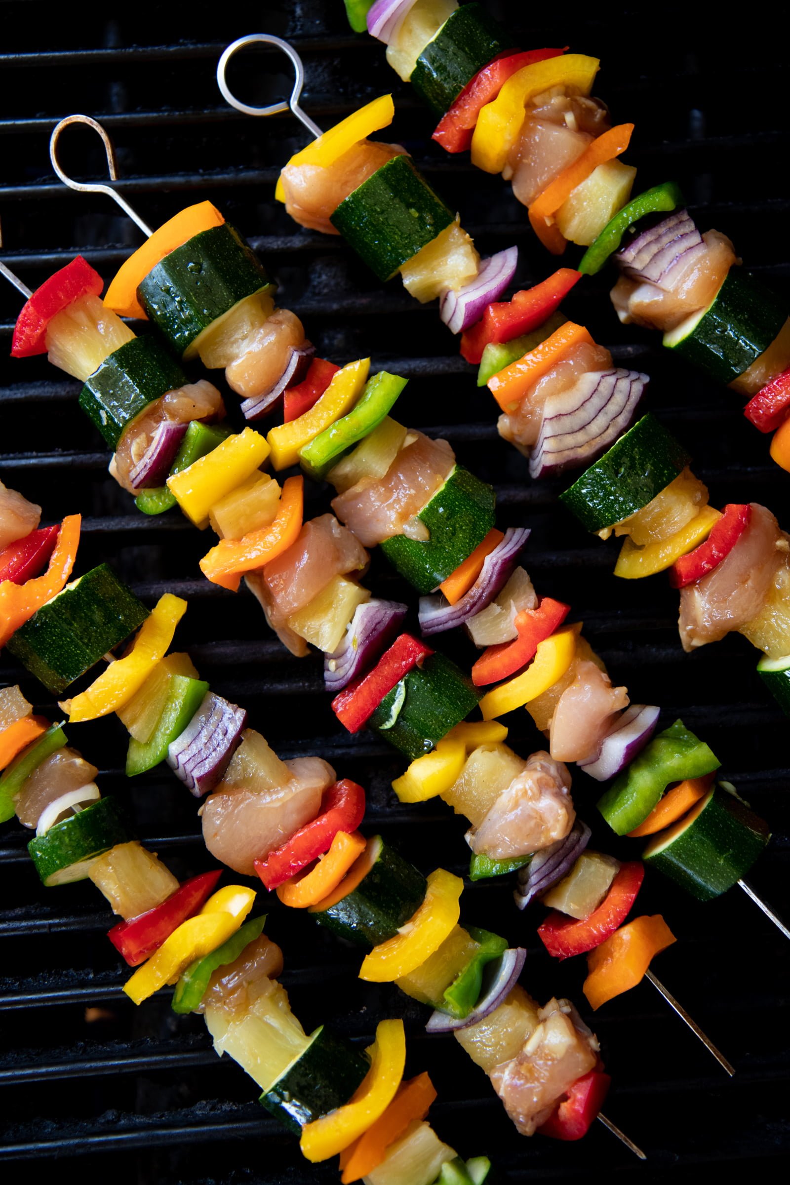 Metal skewers threaded with chicken, vegetables, and pineapple on top of a grill.