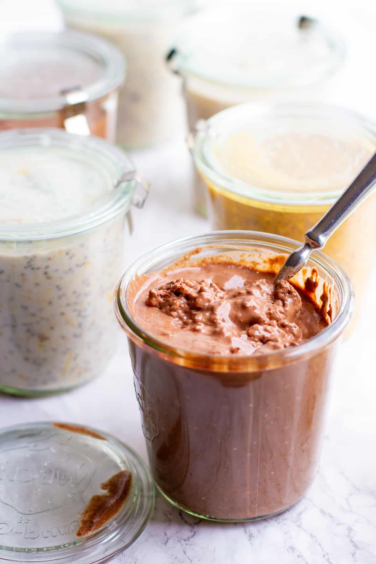 Tight view of a Coconut Chocolate Overnight Oats in a glass jar with a spoon in it.