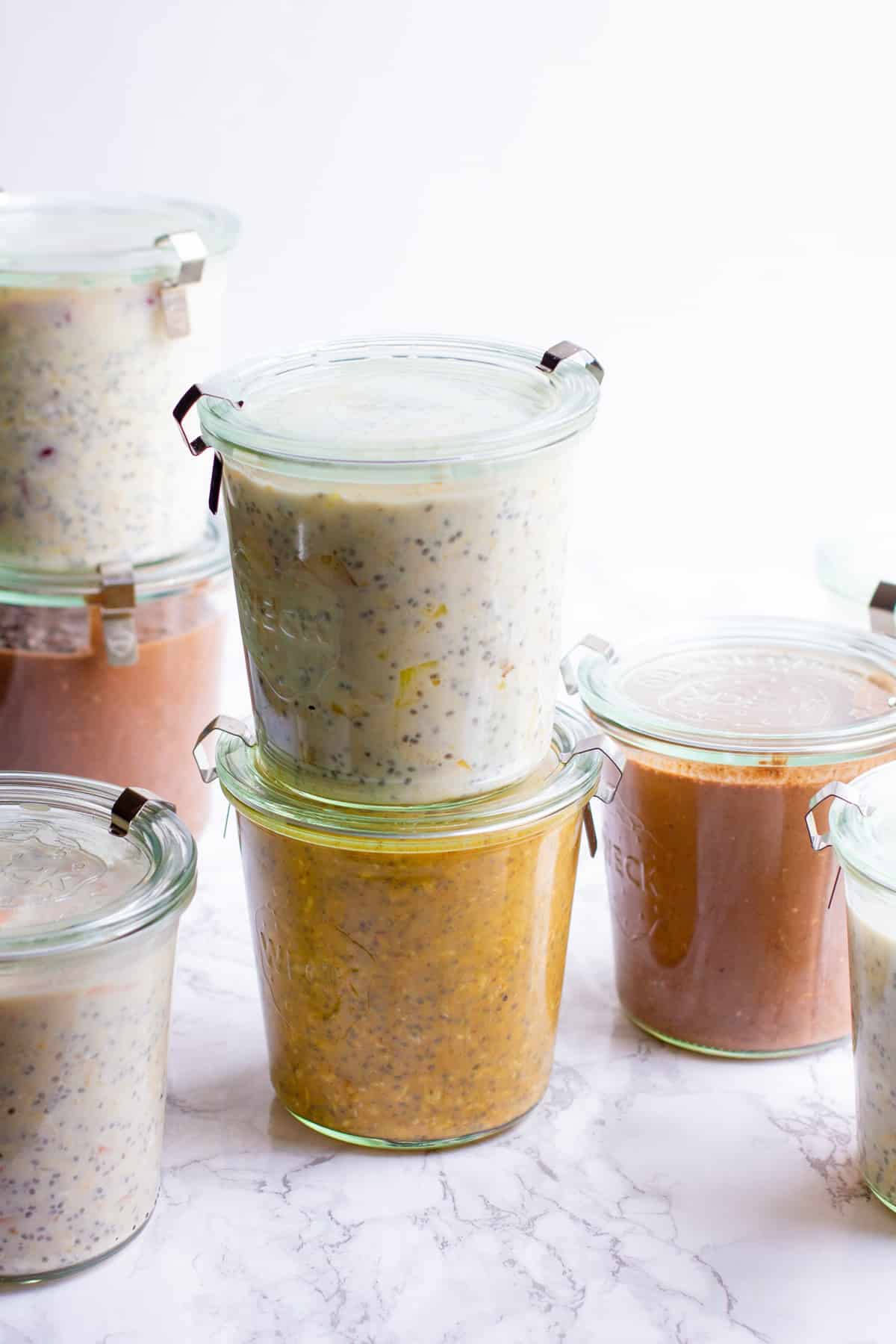 Closed jars of different flavors of overnight oats are stacked against a white background