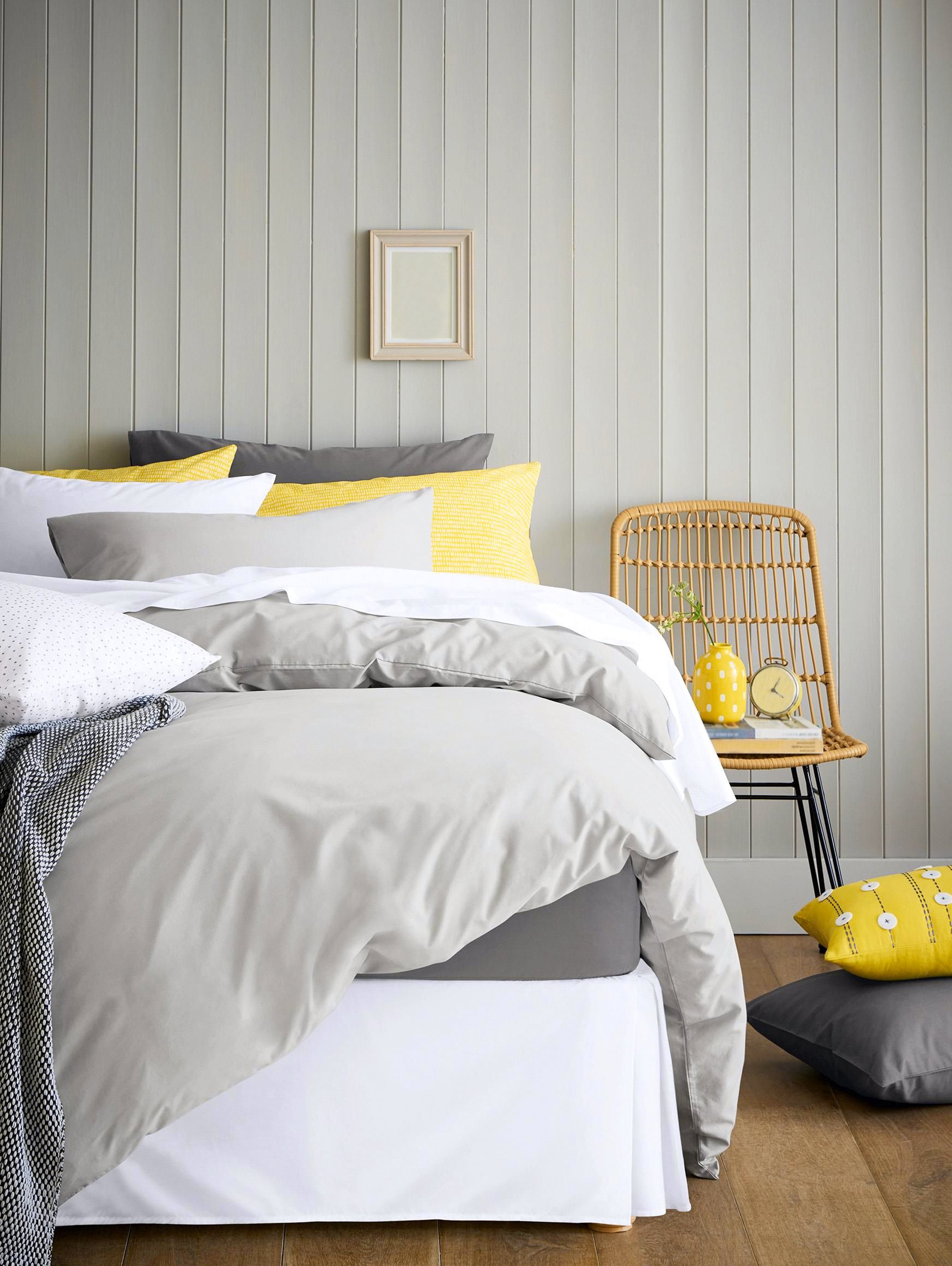 Bed with a grey comforter and white, grey, and yellow pillows.