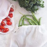 Three white cotton voile reusable produce bags filled with kale, cherry tomatoes, and green beans.