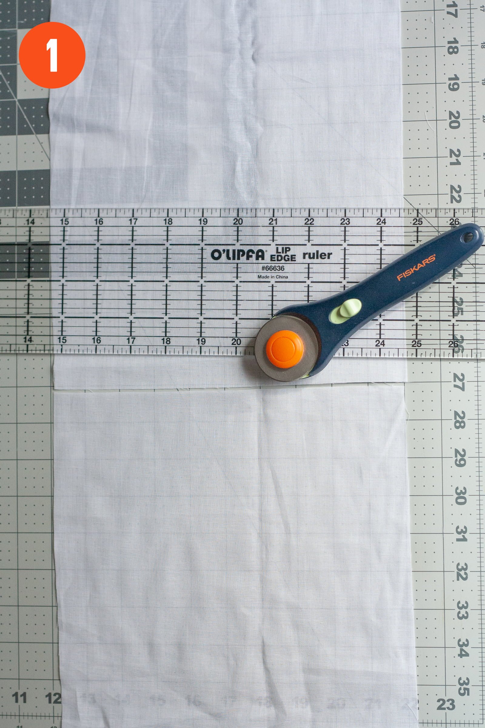 Rotary cutter and ruler on top of a cut piece of cotton voile. Labeled with a "1"