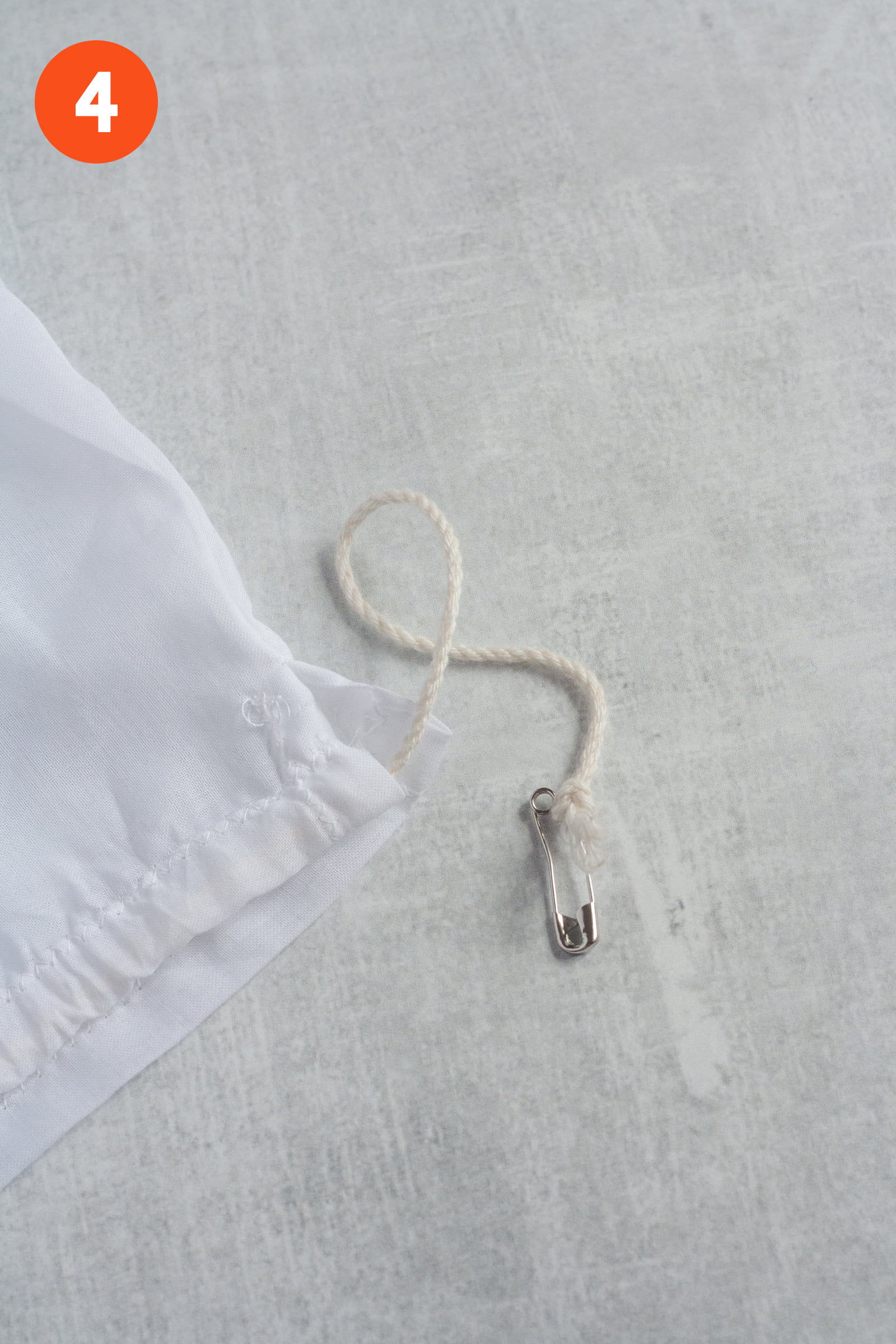 Safety pin with cording tied around it, to help thread the drawstring. Labeled with a 4.