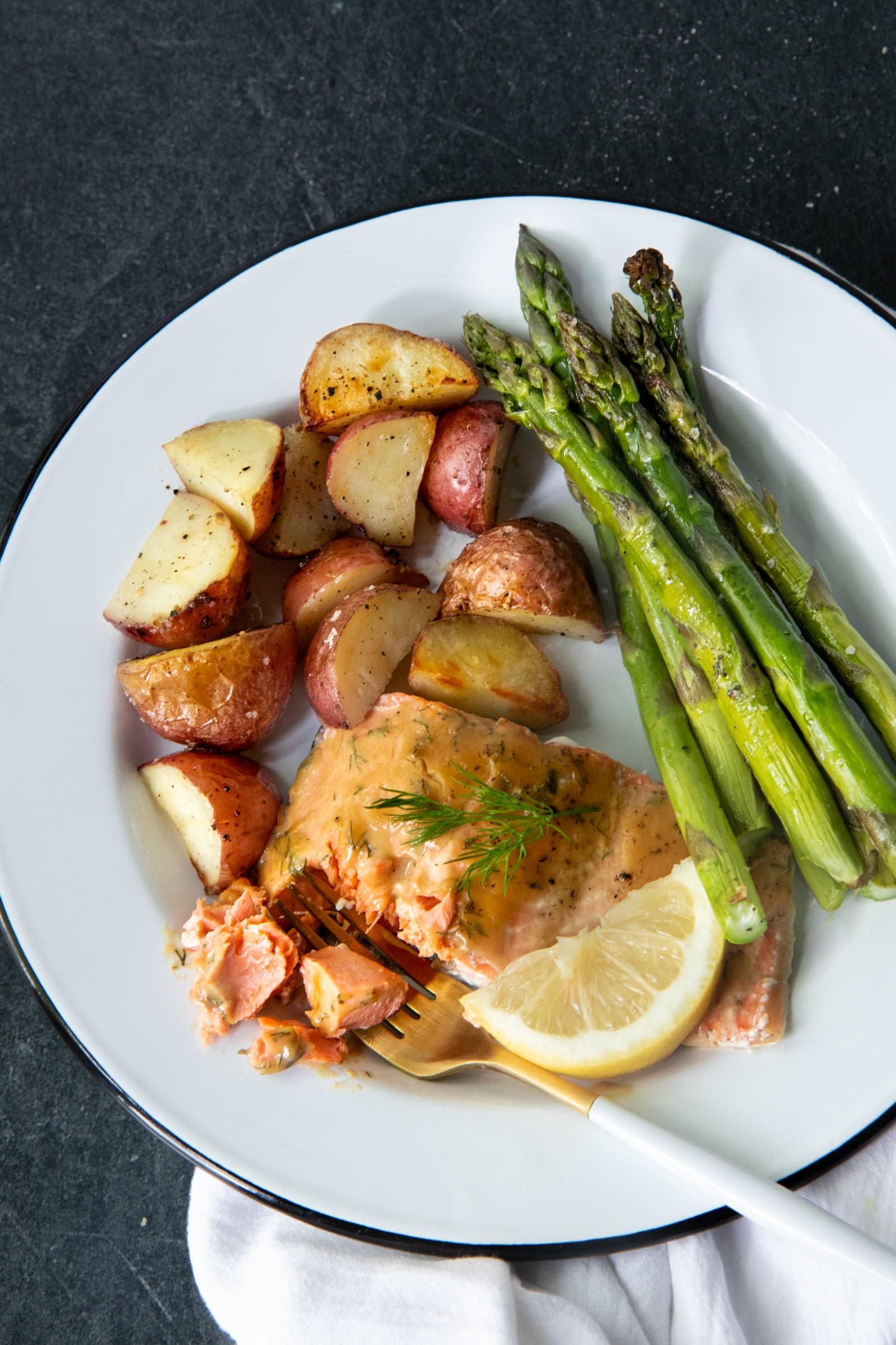 Overhead of roasted maple glazed salmon, asparagus, and potatoes on a white plate with a fork.
