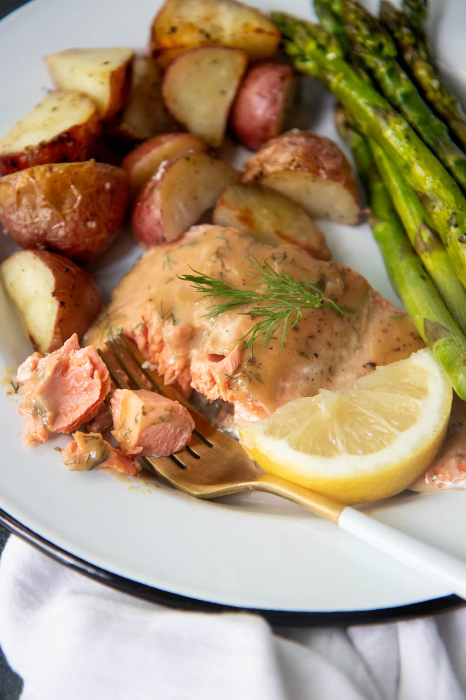 Close-up of roasted maple glazed salmon, asparagus, and potatoes on a white plate with a white and gold fork.