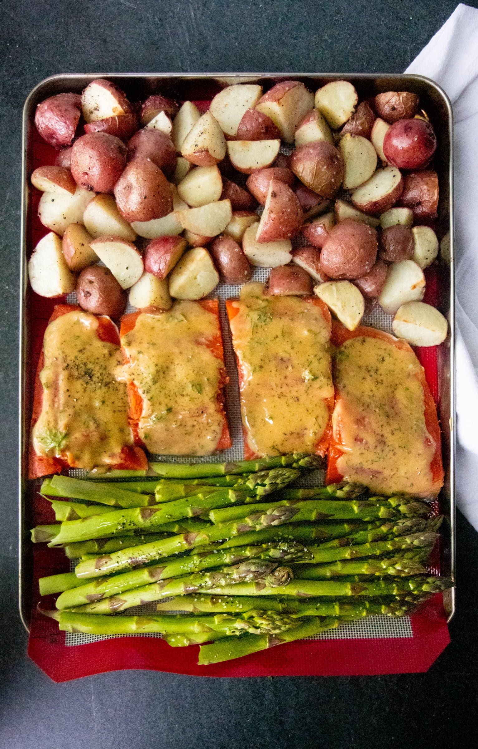 Sheet pan covered with a silicon baking sheet, salmon, asparagus, and potatoes, ready to be cooked.