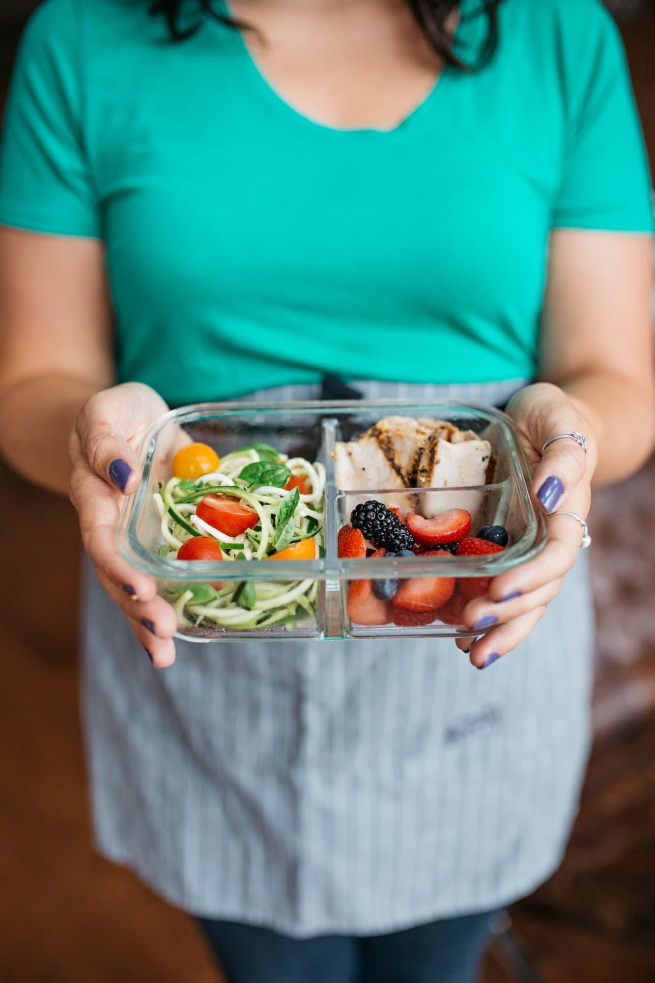 Close-up of a woman holding a divided glass container filled with a prepped meal.