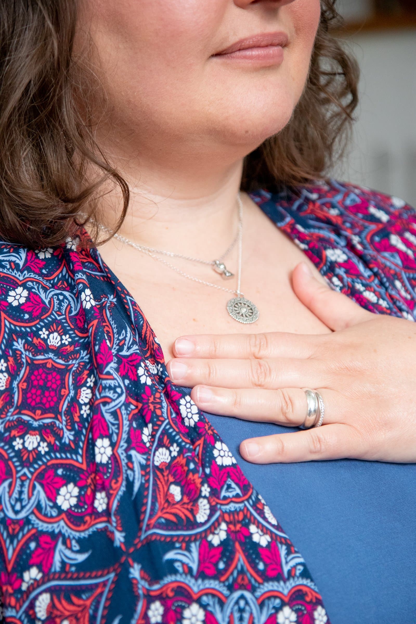 Close up of a woman's torso. She has her hand on her chest as she meditates.