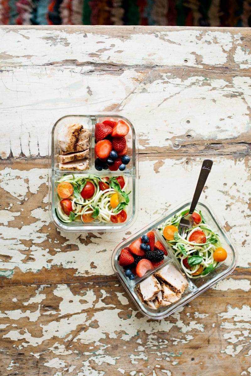 Two divided glass containers filled with a meal prep lunch - chicken, berries, and vegetables.