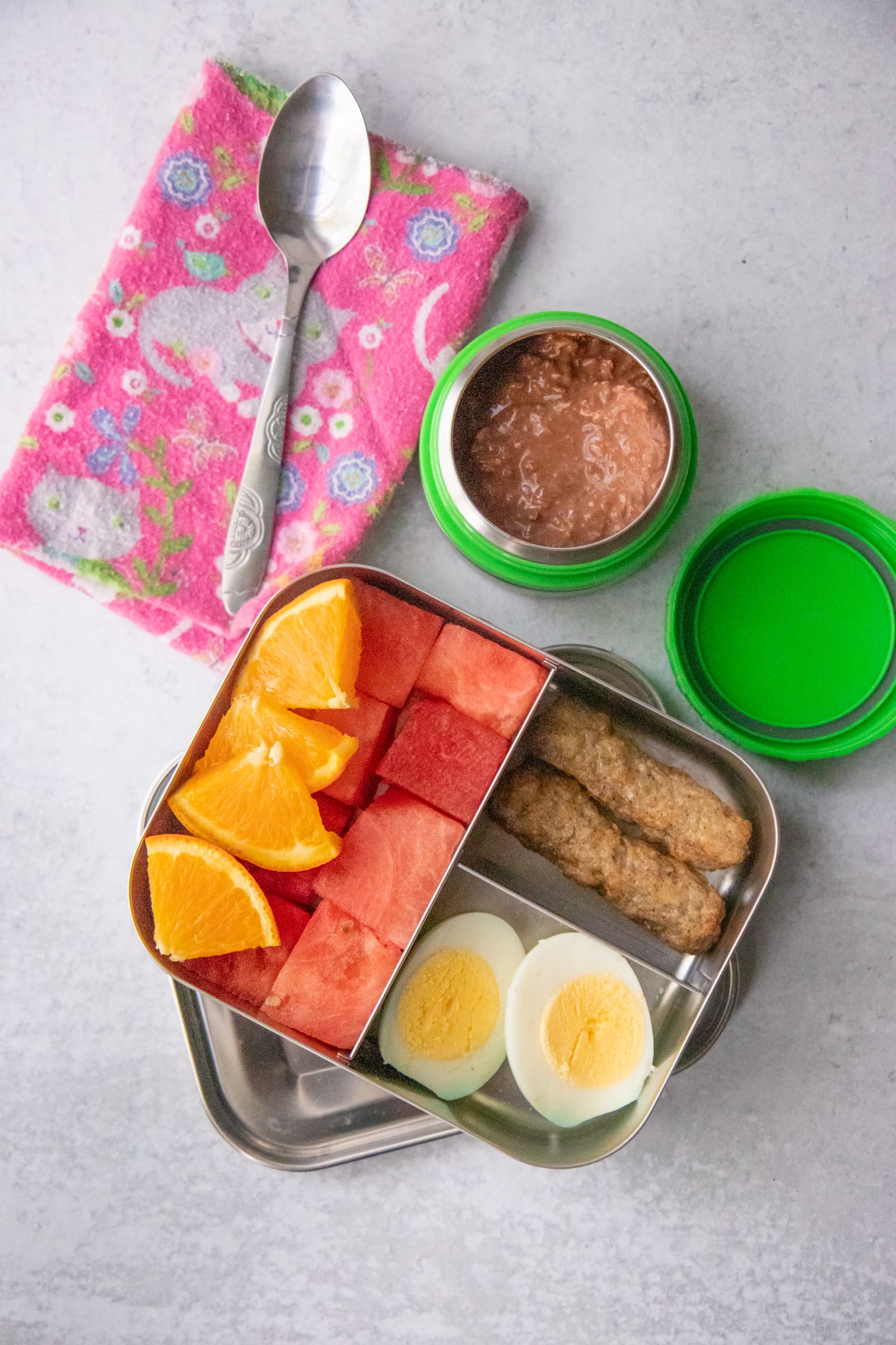 Waste-free packed lunch of sausage links, hard boiled egg, applesauce, and fruit.