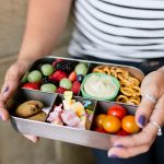 Hands holding a filled bento-style lunch box for a zero-waste lunch