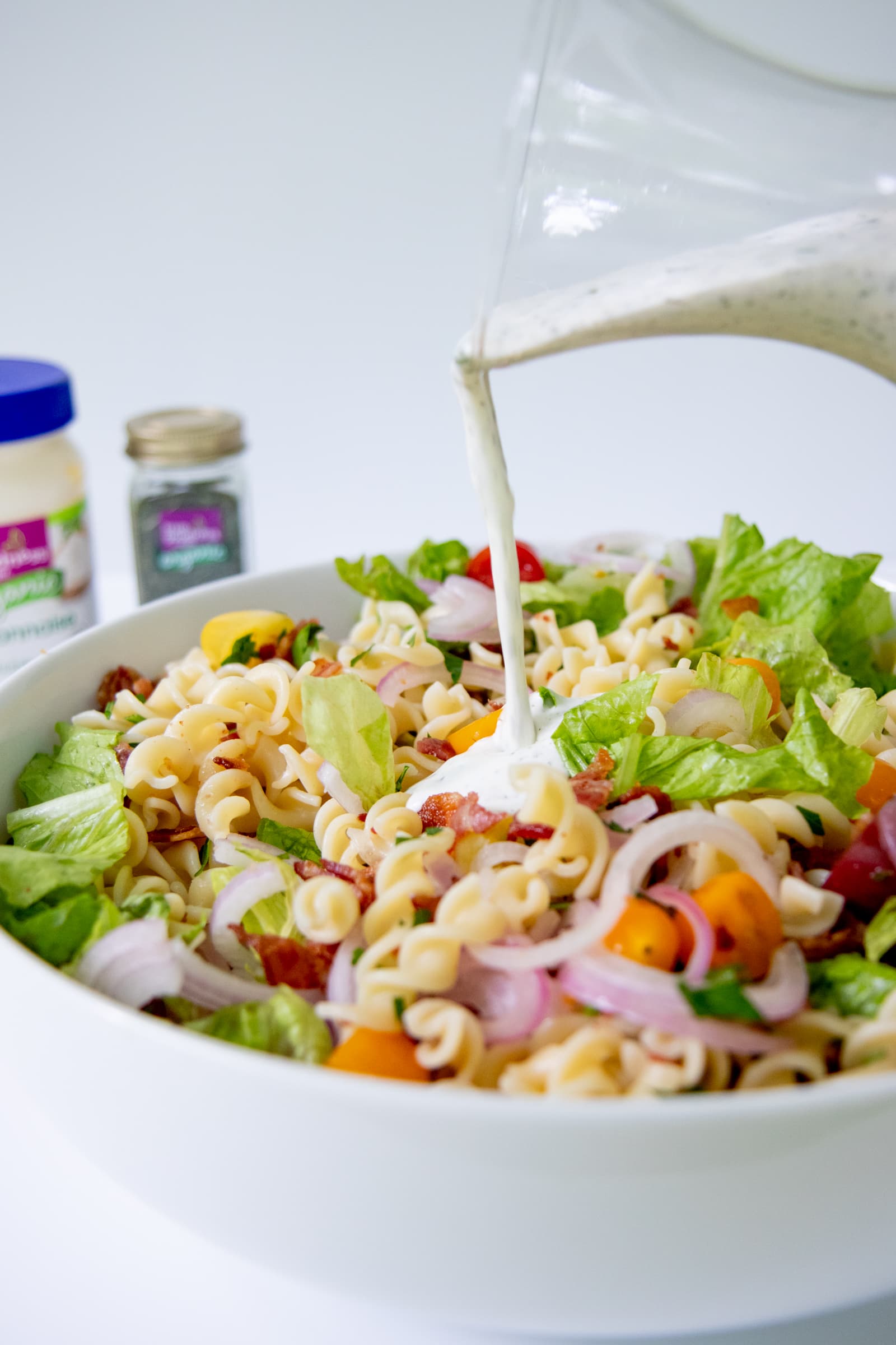 Homemade ranch dressing being poured over a pasta salad