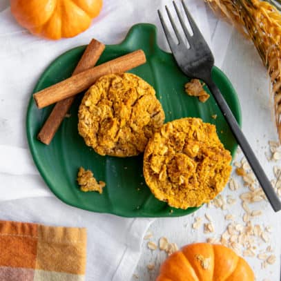 Two Pumpkin Spice Baked Oatmeal Cups on a green plate with cinnamon sticks