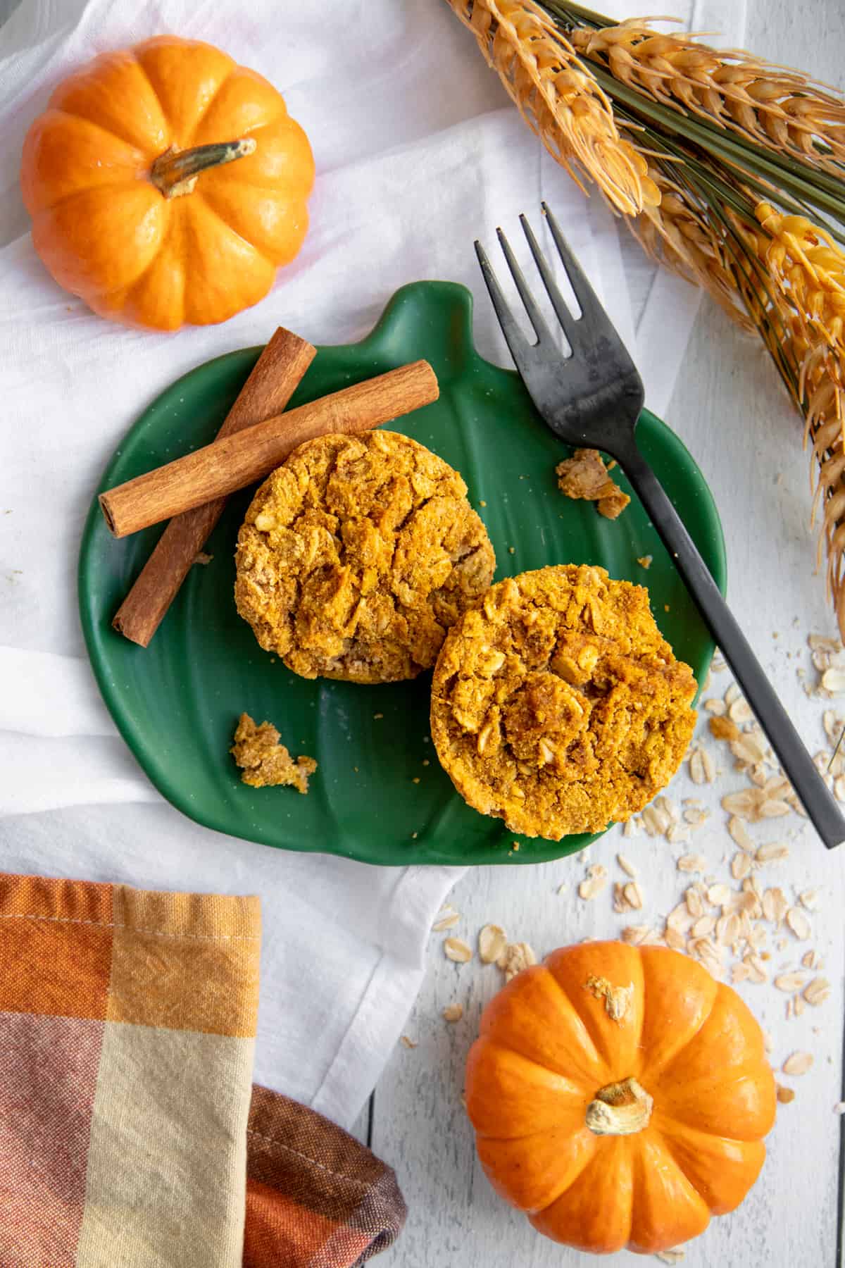 Two Pumpkin Spice Baked Oatmeal Cups on a green plate with cinnamon sticks