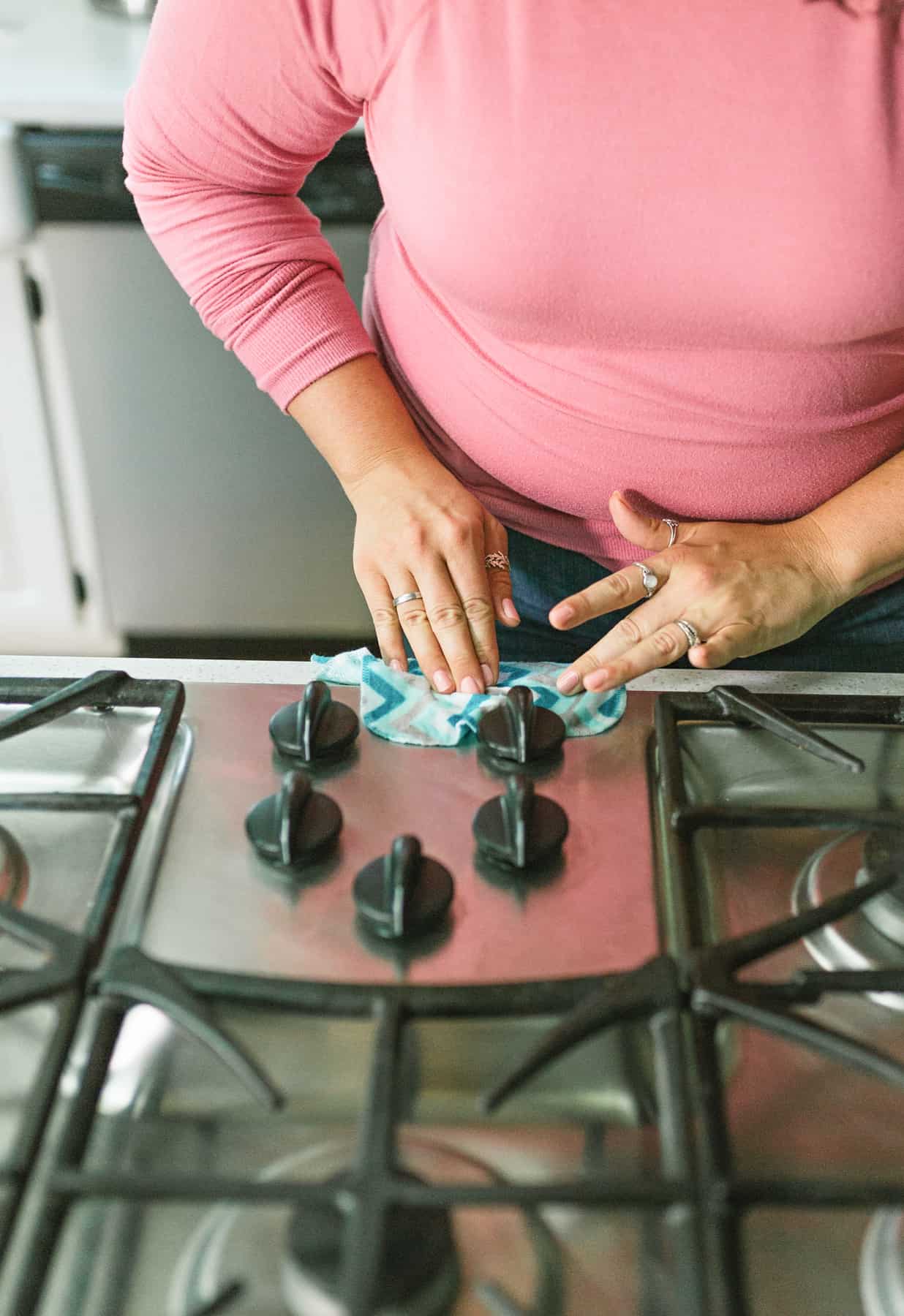 Woman using a reusable cleaning wipe to clean a stovetop.