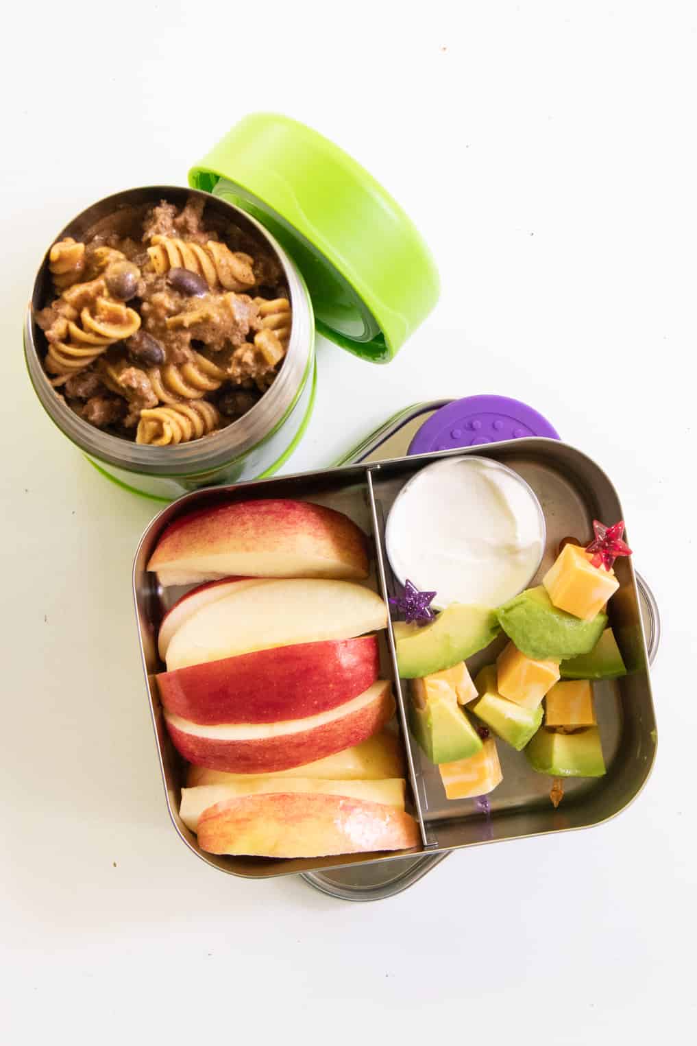 Stainless steel lunchbox with fruit and cheese and avocado skewers, next to a Thermos of taco macaroni skillet.