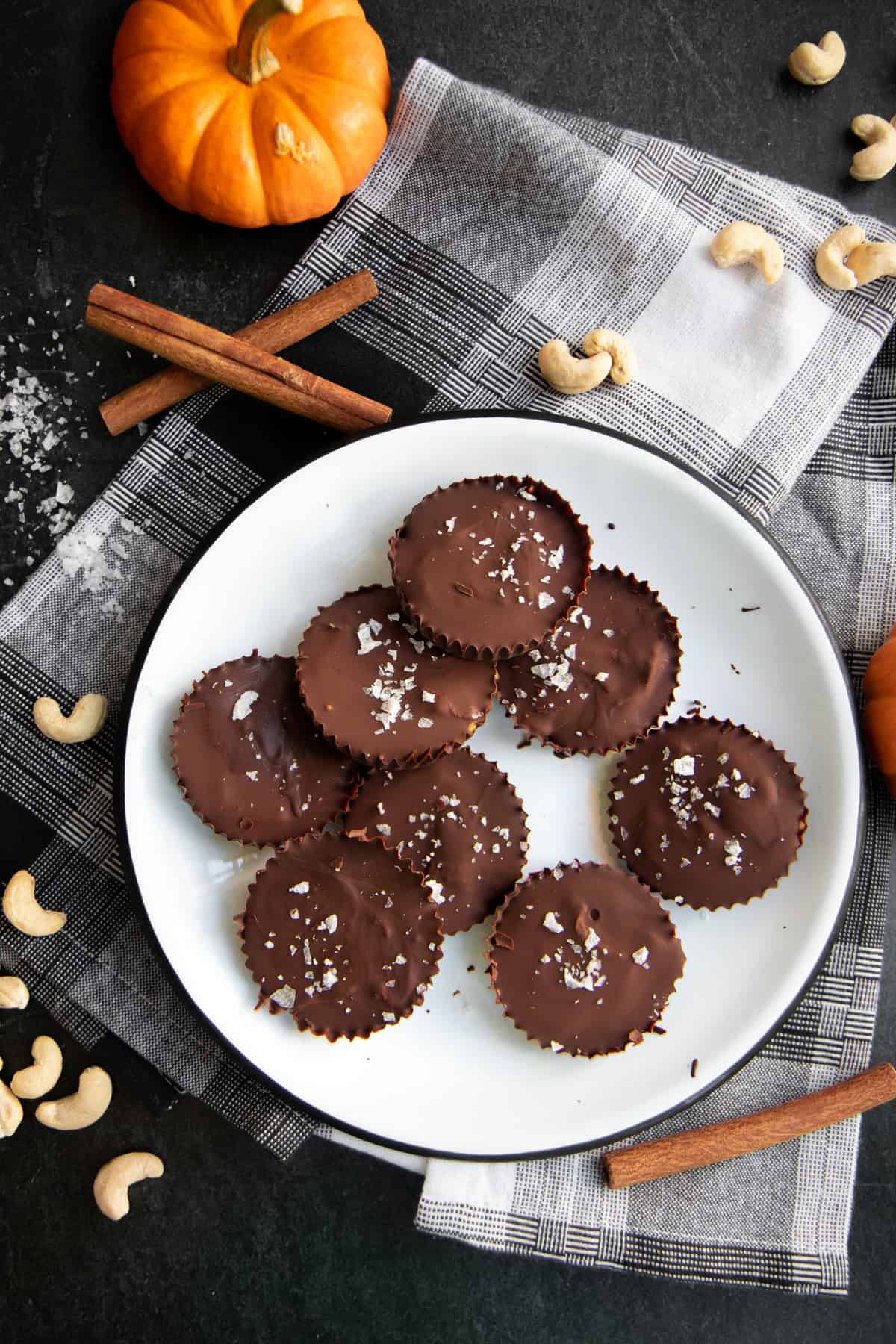 Pumpkin Spice Dark Chocolate Nut Butter Cups arranged on a white plate on top of a plaid background.