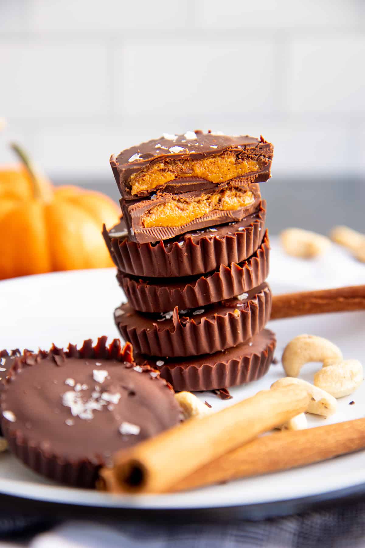 Stack of Pumpkin Spice Dark Chocolate Nut Butter Cups arranged on a white plate. One of the cups is cut in half to show the filling.
