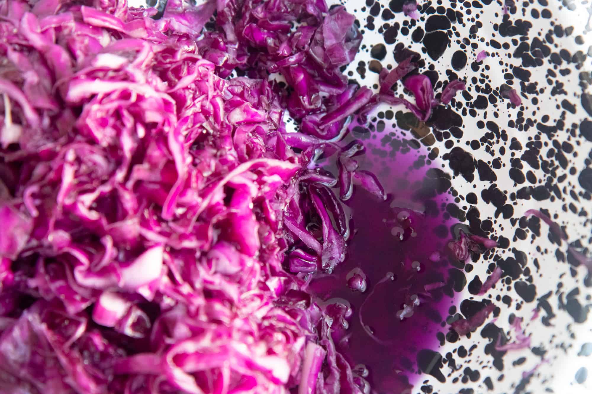 Sliced red cabbage sits in a pool of brine as a step towards making homemade sauerkraut.