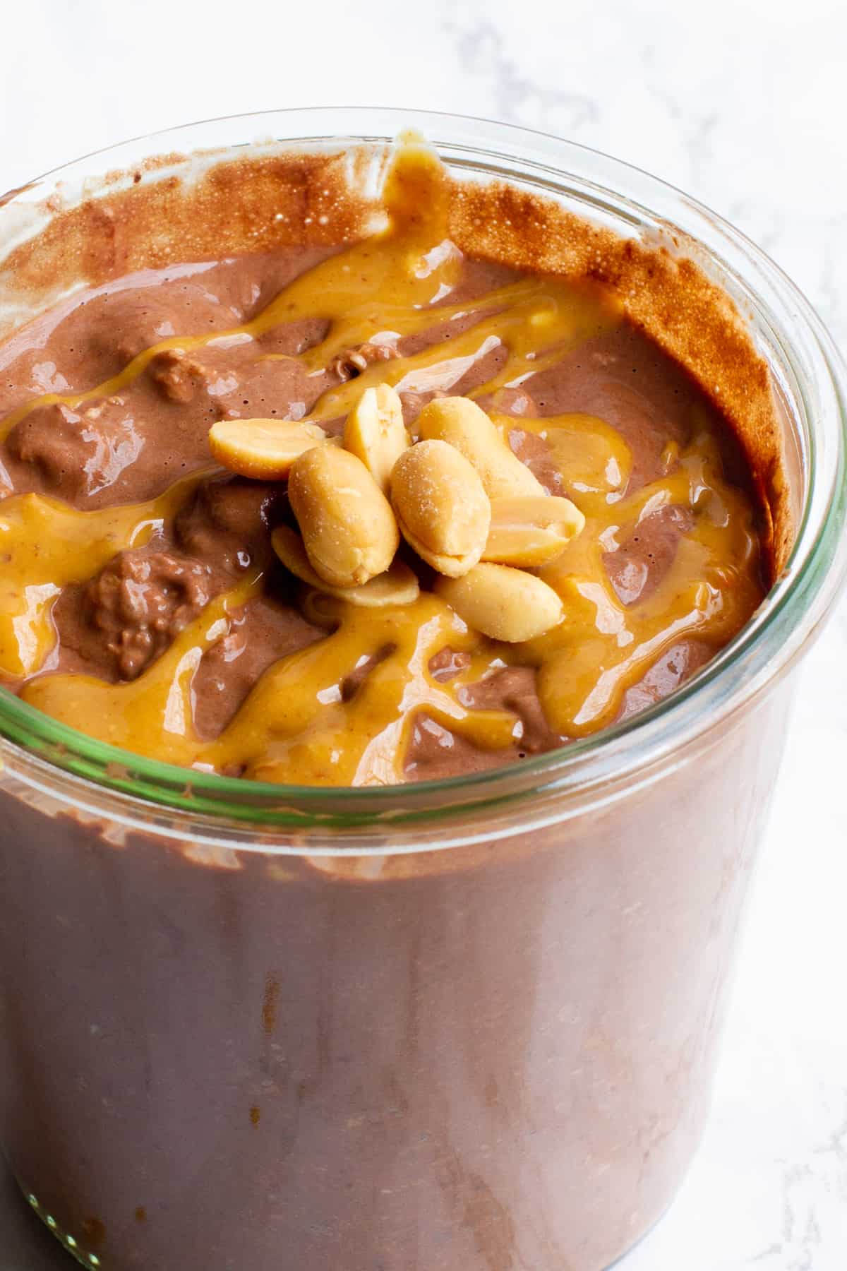 Close up of peanut butter chocolate overnight oats in a glass jar. There are peanuts garnishing the top.