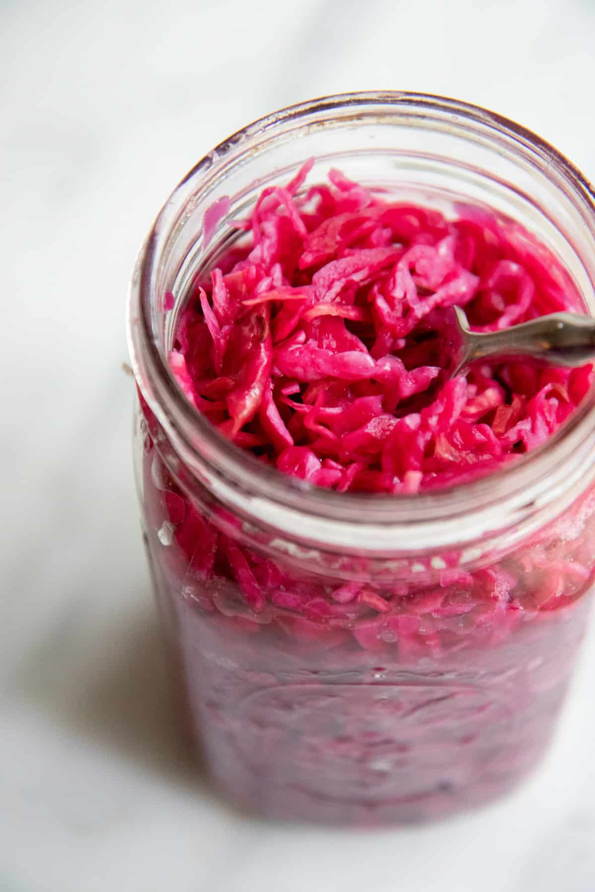 An open jar of finished red sauerkraut, with a fork sitting in the jar.