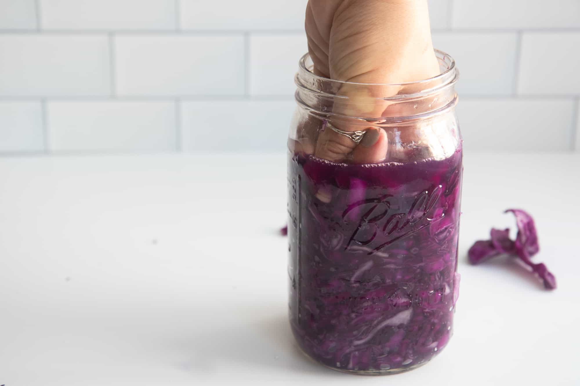 A fist packs sauerkraut into a glass jar.