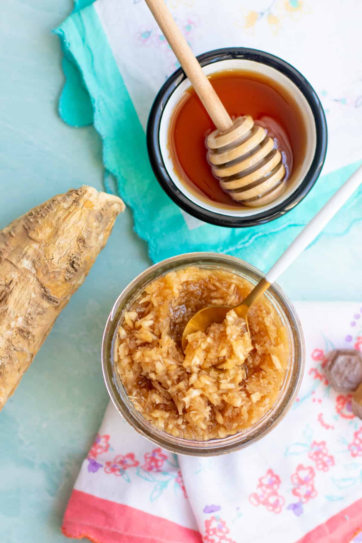 Overhead view of a jar of a natural sinus relief home remedy, next to a whole horseradish root and a small bowl of honey. A spoon dips into the sinus kicker.