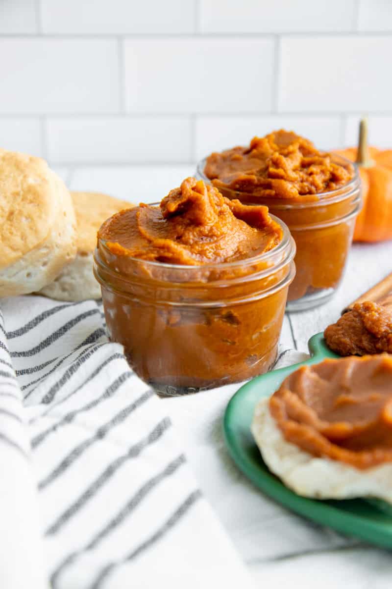 Two glass jars filled with Slow Cooker Pumpkin Butter, next to biscuits and a plate