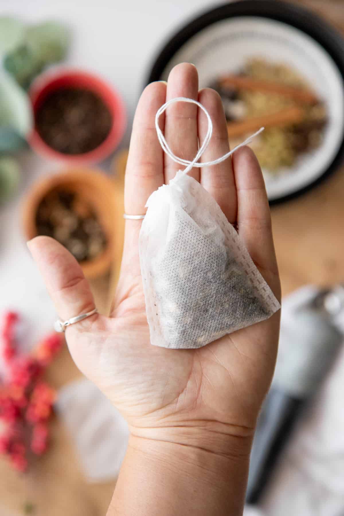 A hand holds a tea bag filled with homemade chai tea blend.