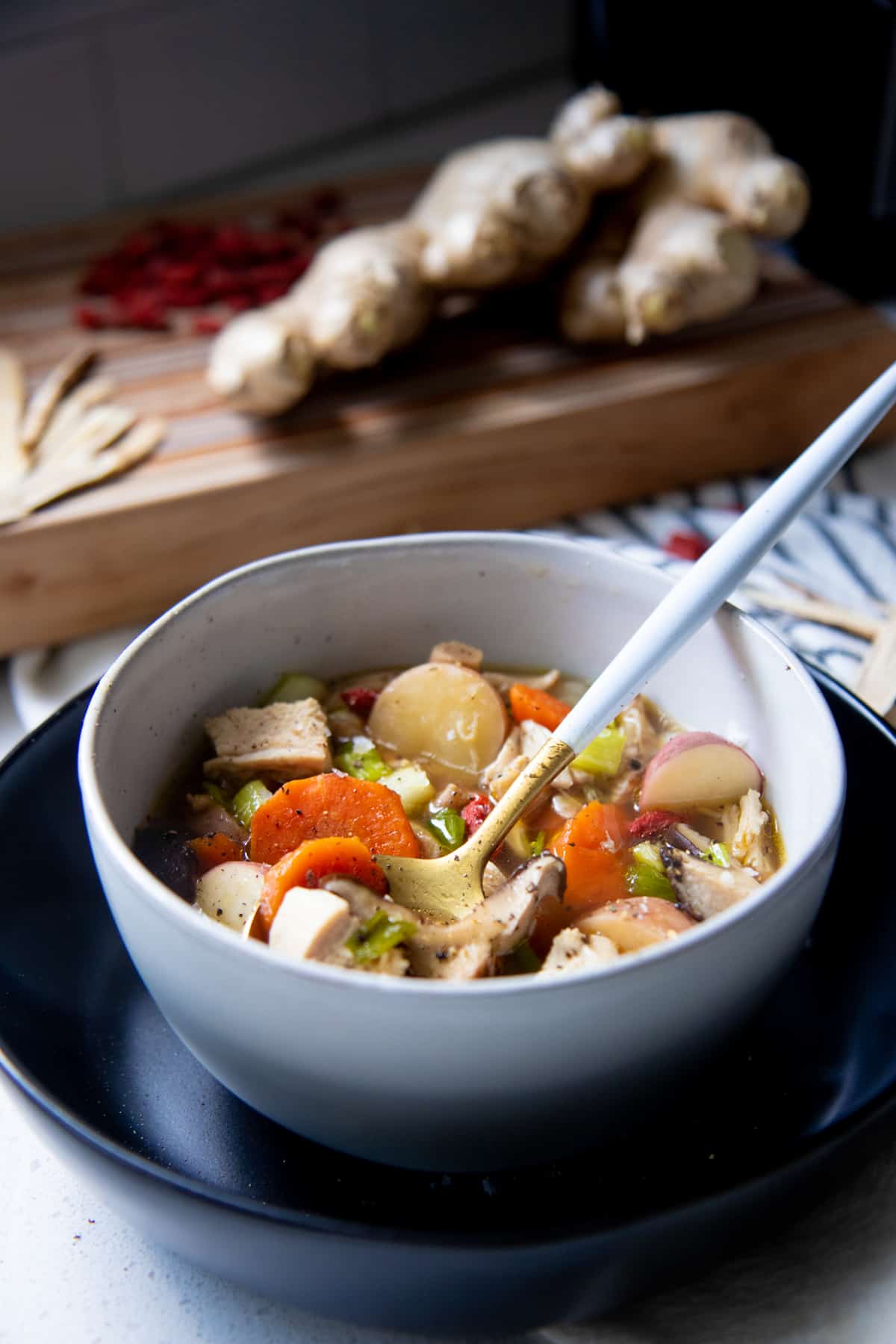 A spoon with a white handle sits in a white bowl full of herbal chicken soup.