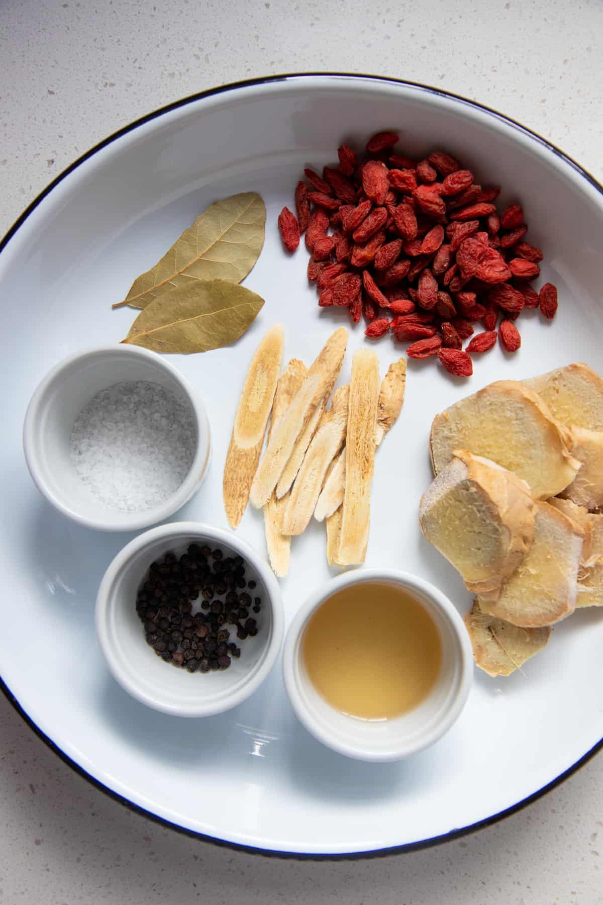 Ingredients are laid out on a white plate, including Chinese herbs and bay leaves.