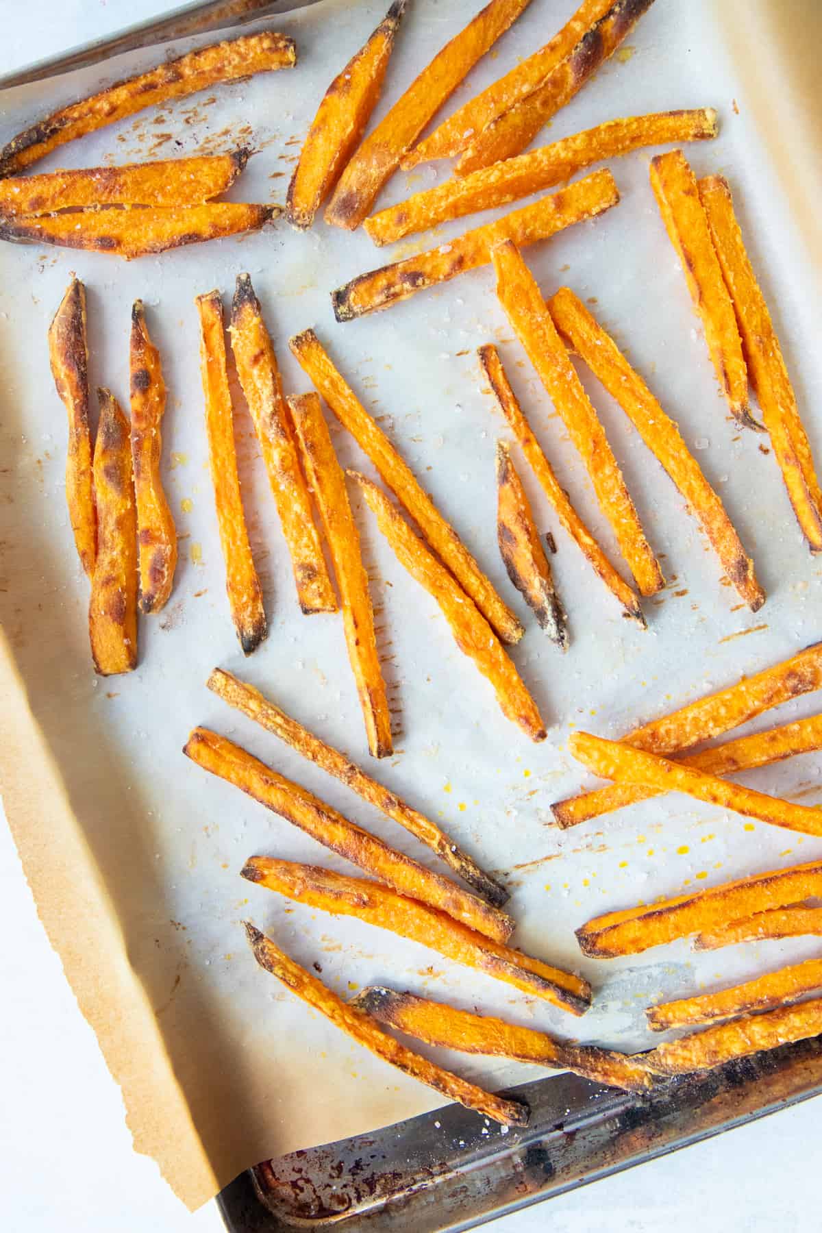 Baked sweet potato fries spread out on a baking sheet lined with parchment paper.