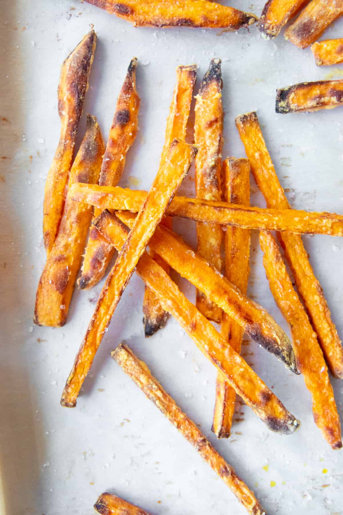 Sweet potato fries piled on top of each other on parchment paper.
