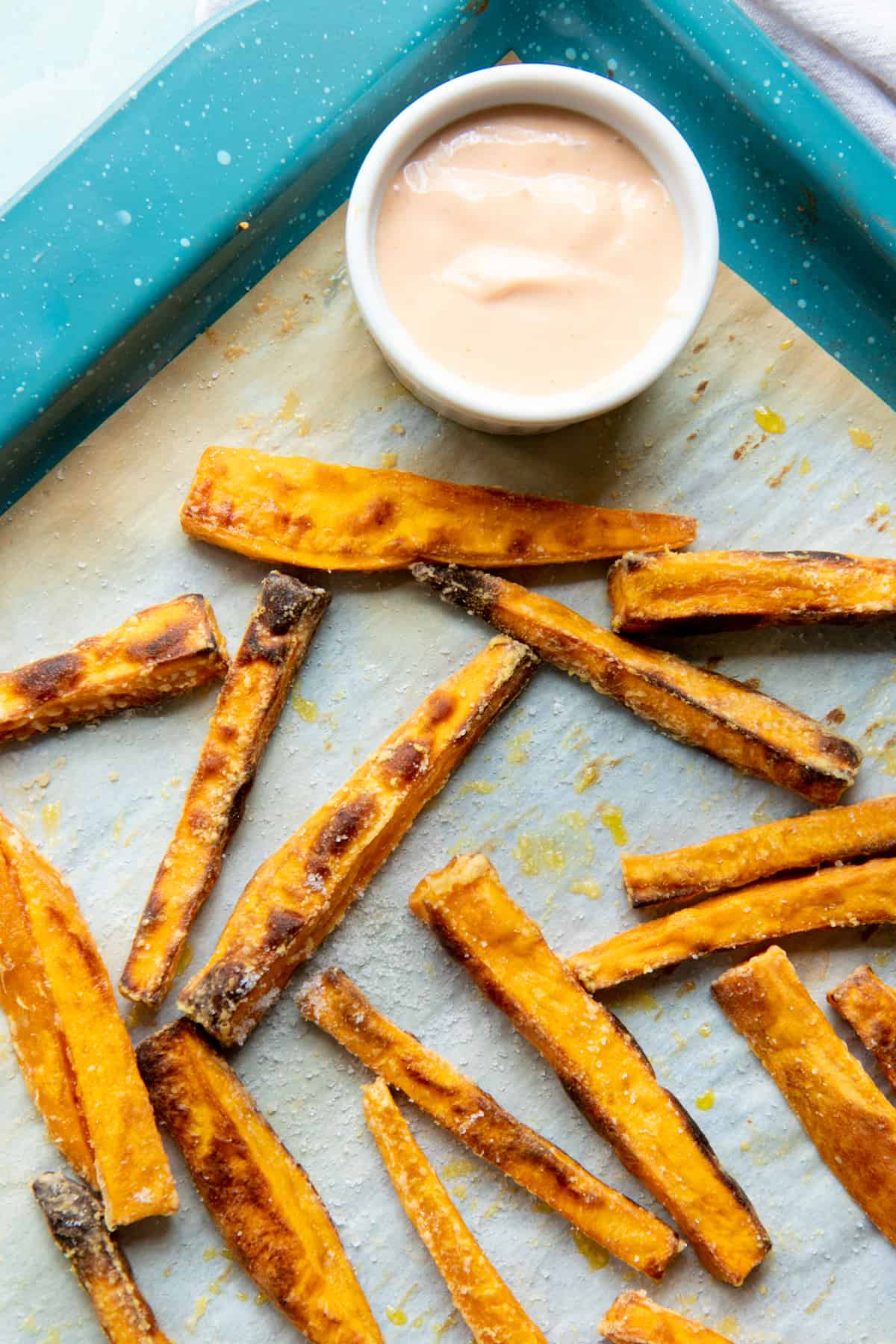Baked fries sit on a baking sheet next to a small ramekin of dipping sauce.