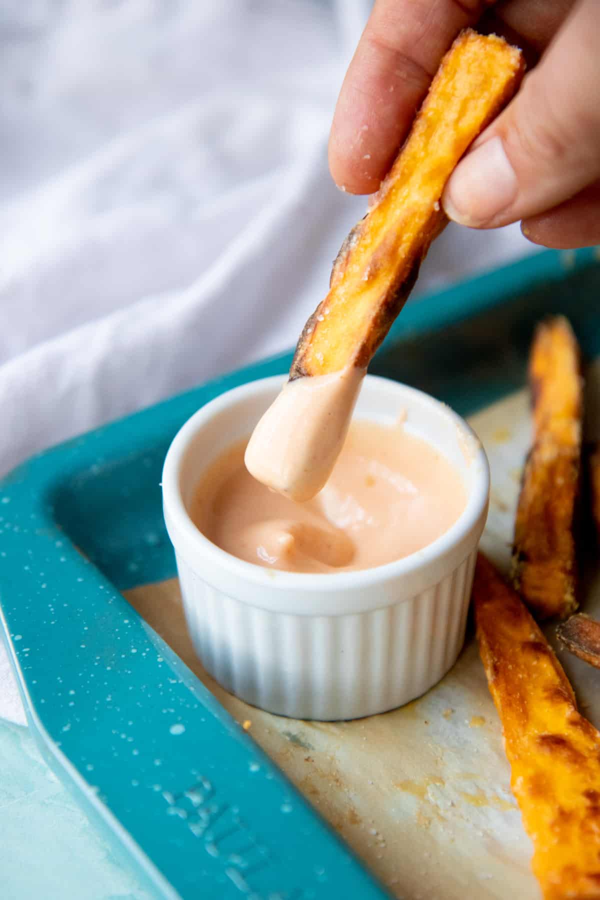 A sweet potato fry dips into a small ramekin of dipping sauce.