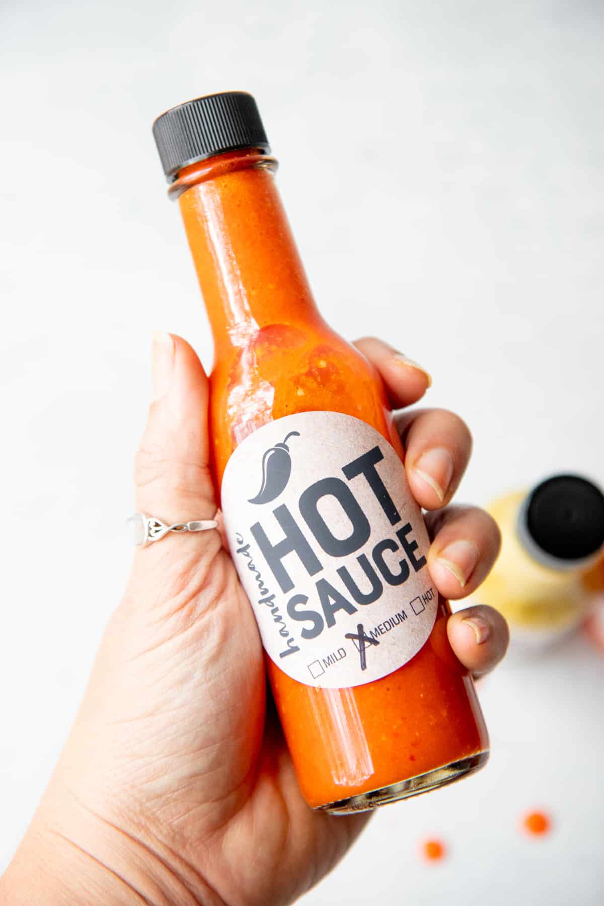 A hand holds out a bottle of red hot sauce.