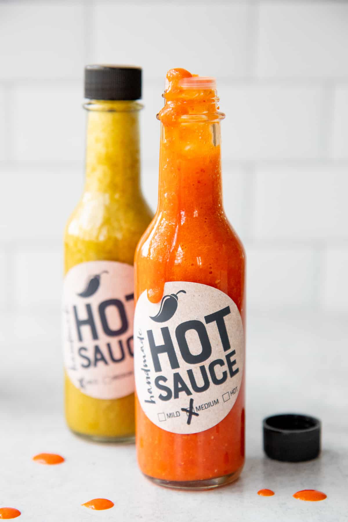 Two bottles of labeled hot sauce sit on a counter. One of the bottles is open.