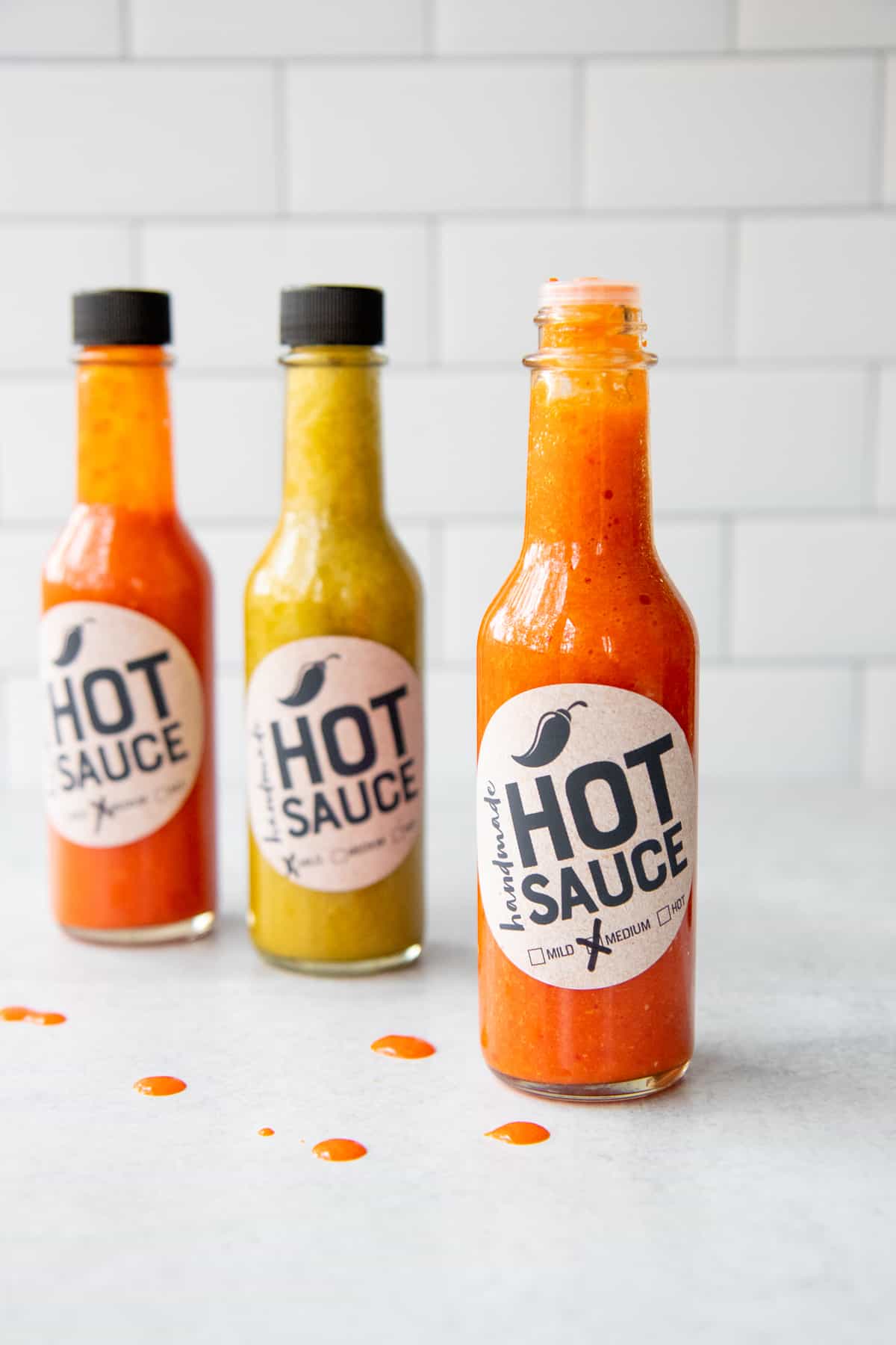 Three bottles of labeled hot sauce sit on a counter. One of the bottles is open.